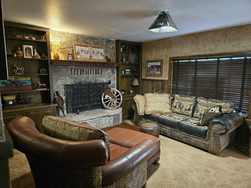 Great room with a floor-to-ceiling stone fireplace topped by a cedar mantel, built-in bookcases on either side, leather club chair with ottoman, and a wagon-wheel art piece on the hearth